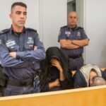 a group of police stand while distressed people sit with their heads down near them