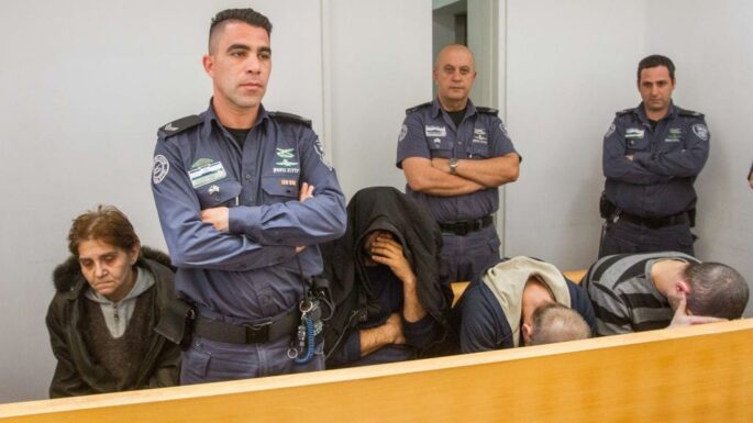 a group of police stand while distressed people sit with their heads down near them