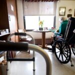 A female nursing home resident in a wheelchair sits near a window in her room