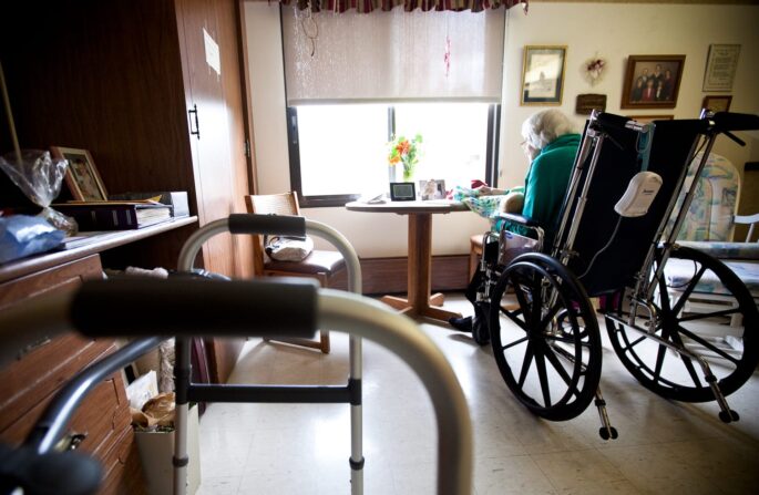 A female nursing home resident in a wheelchair sits near a window in her room