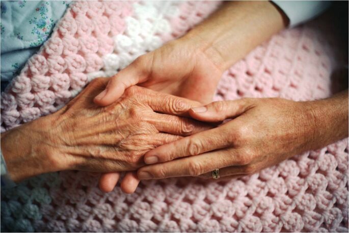 an older person's hand holds a younger person's hands