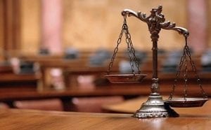 A close-up of the scales of justice resting on a wooden desk inside a courtroom.