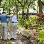 An adult man helps an elderly man walk in a garden