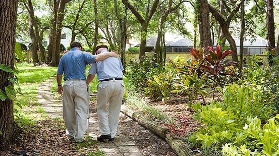 An adult man helps an elderly man walk in a garden