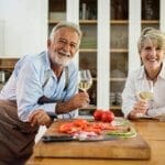 Two older adults enjoy wine and vegetables in their kitchen