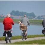 Three older adults ride bicycles near a lake