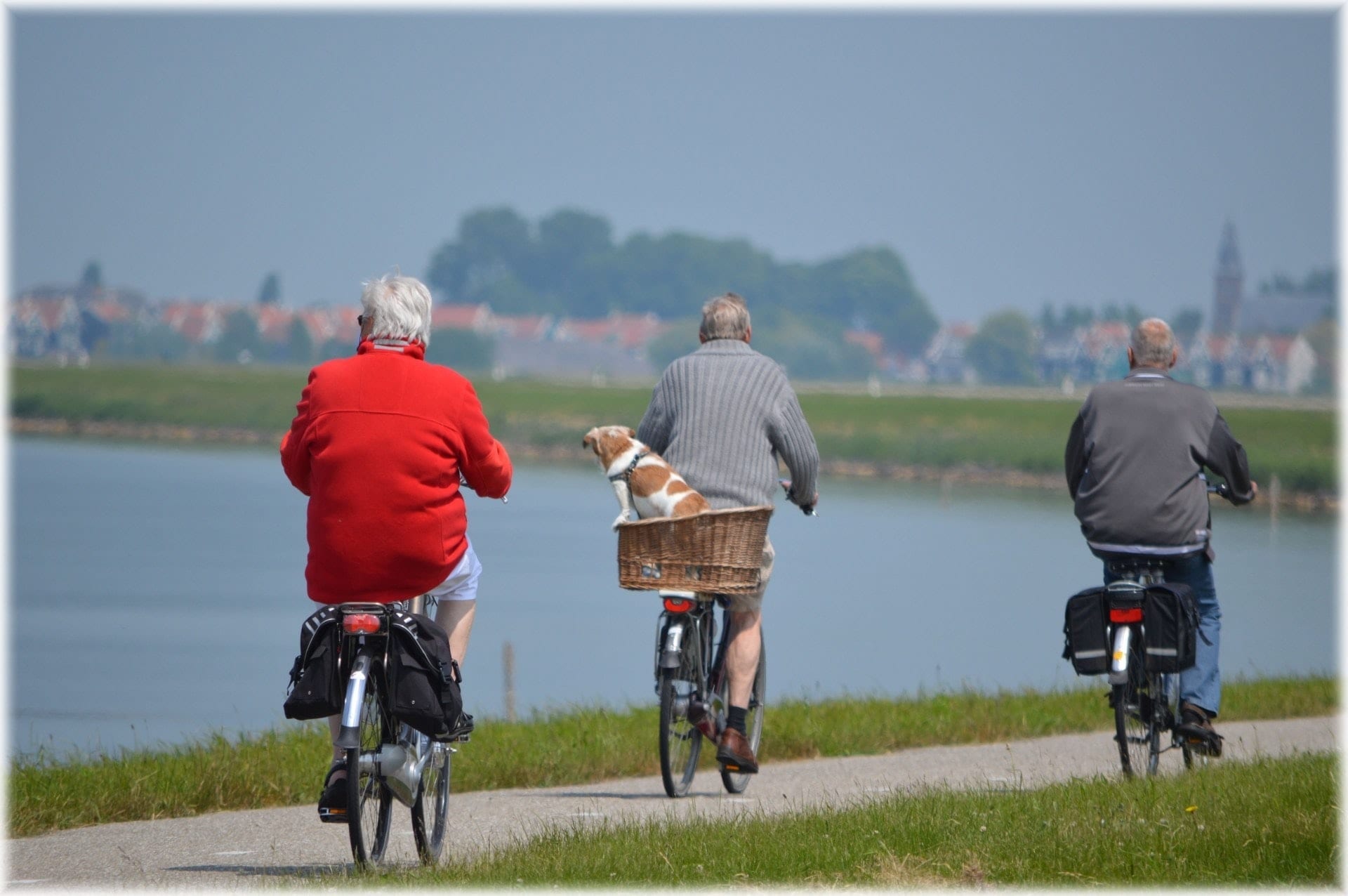 Three older adults ride bicycles near a lake