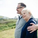 An adult son puts his arm around his elderly mother in a field