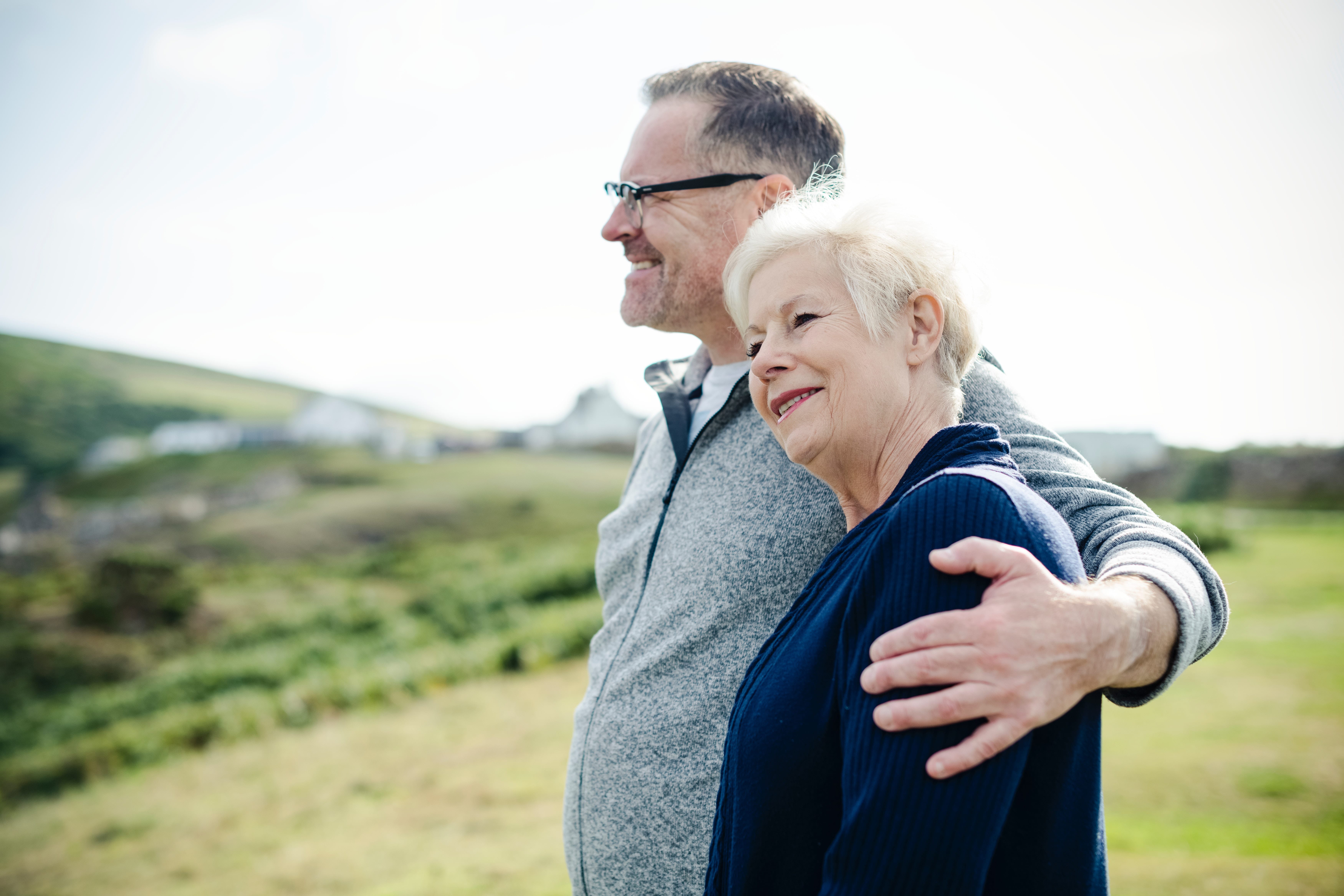 An adult son puts his arm around his elderly mother in a field