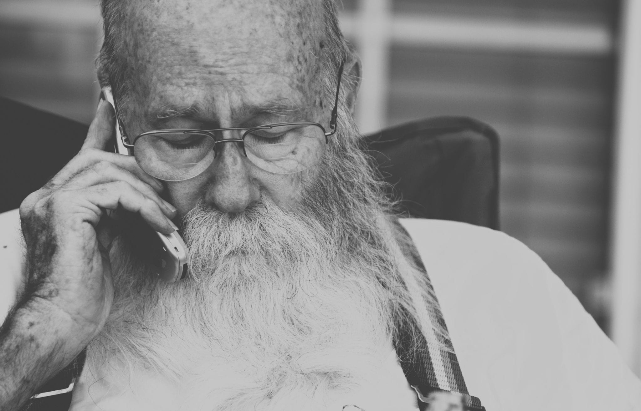 An older man with a beard and glasses talks on the phone