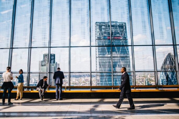 a businessman walks near a large window with a city backdrop