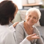 A woman talks to an old lady in a nursing home.