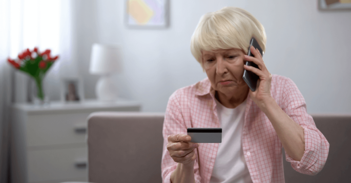 elderly woman looking at credit card and talking on the phone