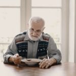 An old man eats soup at a table.