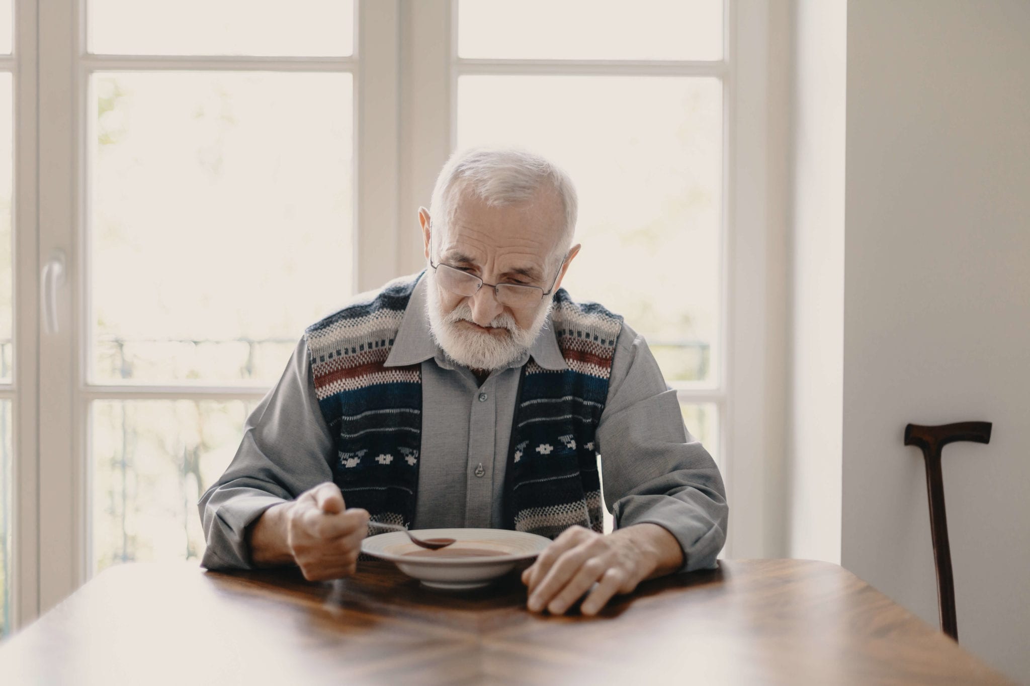 An old man eats soup at a table.