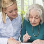 A middle-aged woman helps an elderly woman sign some documents