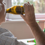 An elderly man drinks from a bottle of alcohol
