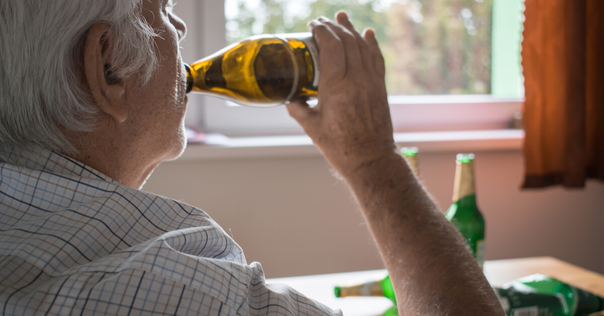 An elderly man drinks from a bottle of alcohol