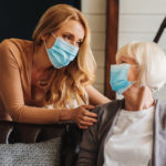 an older woman meets with her adult daughter, and both wear facemasks