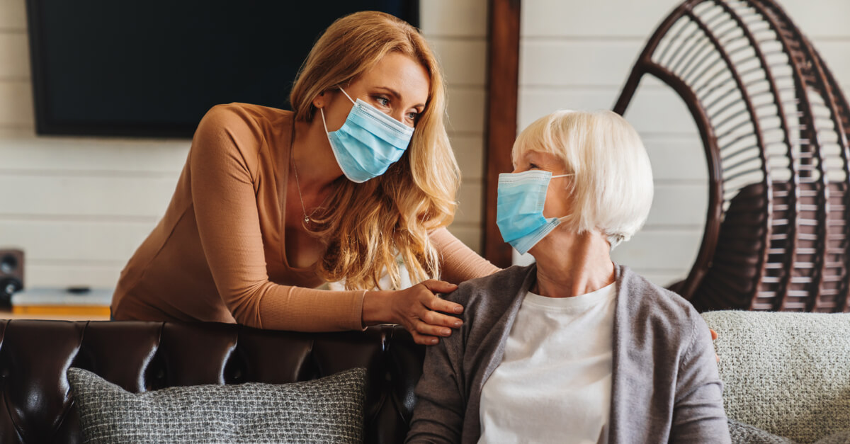an older woman meets with her adult daughter, and both wear facemasks