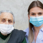 an older adult stands with a younger woman, and both are wearing face masks
