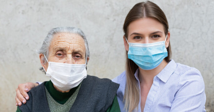an older adult stands with a younger woman, and both are wearing face masks