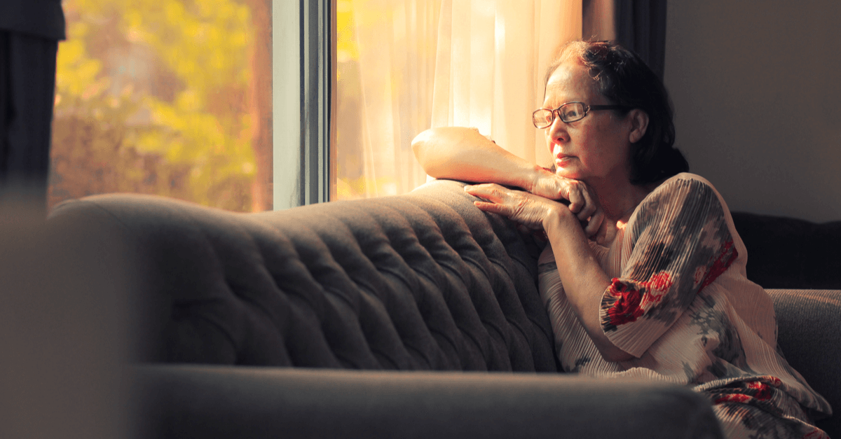 an older woman with glasses sadly sits on a couch