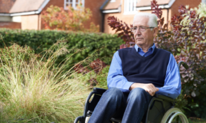 An older man in a wheelchair sits outside with a concerned look on his face