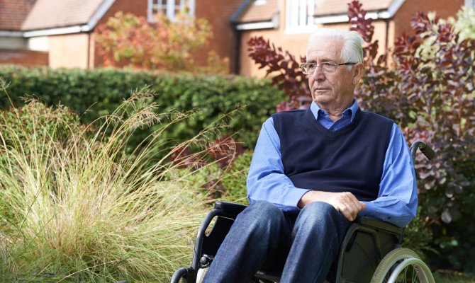 A man using a wheelchair looks worried as he sits outside a nursing home.