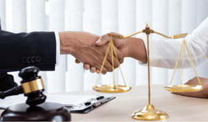Two people shake hands at a desk with gavel and scales of justice