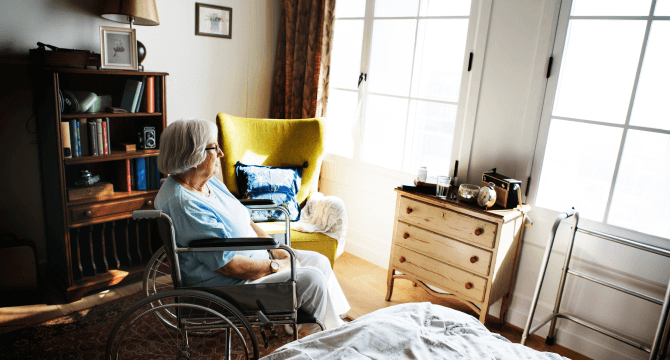 A female nursing home patient in a wheelchair sits in a room and looks out the window