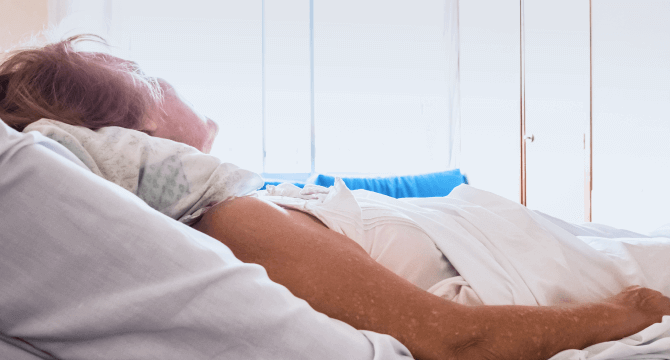 An older woman laying in a bed in a nursing home. 