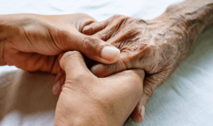 Two younger people holding the hand of an older person. The image is a closeup so only the hands of the people are visible.