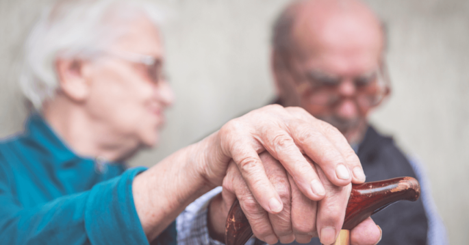 two seniors hold hands over a cane