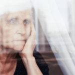 An older woman sits sadly behind a window
