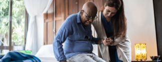 an older man is helped out of bed by a nurse