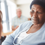 an older woman sits in a nursing home and looks at a nurse in the foreground