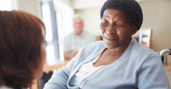 an older African American woman sits in a nursing home and looks at a nurse in the foreground
