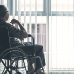 an older man in a wheelchair sits and looks outside a window