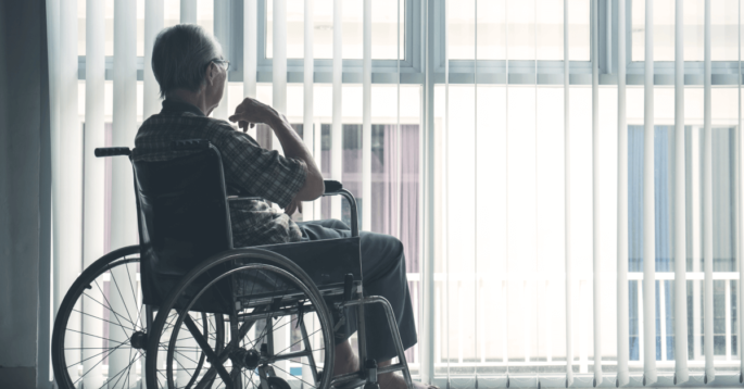 an older man in a wheelchair sits and looks outside a window