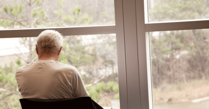 Elderly person sits alone looking out window