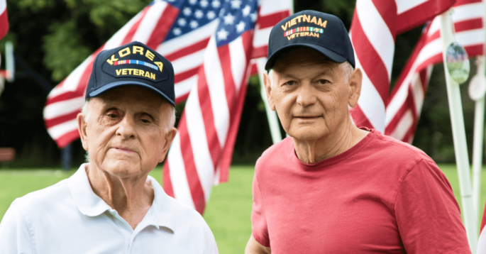 two veterans stand in front of flags