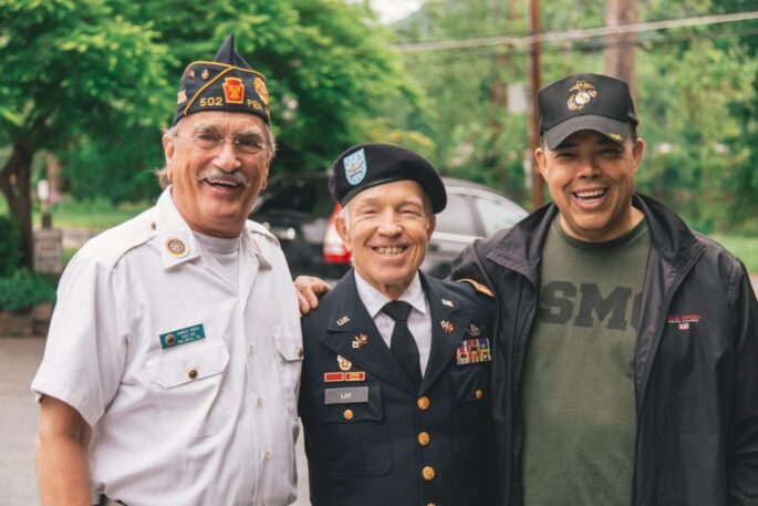Three older male veterans smile together outside