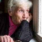 an elderly woman stares out a window and looks concerned