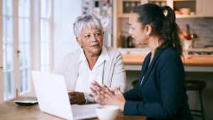 A nursing home lawyer talks with her client at a kitchen table with a laptop open.