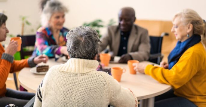 A group of different types of senior citizens sit at a table while appearing to be social.