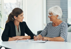 A nursing home lawyer discussing documents with an older woman at a table.
