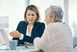 A nursing home abuse attorney meets with a client and reviews materials on a laptop.