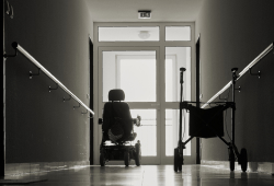 A wheelchair and walker sit in an empty nursing home hallway.