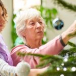 A nursing home resident hangs an ornament on a Christmas tree